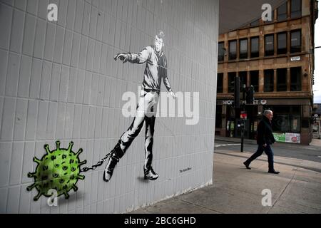 Eine Person geht an einem Kunststück des Künstlers vorbei, das als Rebel Bear bekannt ist, nachdem es an einer Wand in der Bath Street in Glasgow auftauchte. Die neue Ergänzung zu Glasgows Straßenkunst erfasst die globale Coronavirus Krise. Das Stück zeigt einen Mann, der eine Kette mit einem daran befestigten Keim zieht, während Großbritannien sich in einem Lockdown fortsetzt, um die Ausbreitung des Coronavirus einzudämmen. Stockfoto