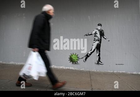 Eine Person geht an einem Kunststück des Künstlers vorbei, das als Rebel Bear bekannt ist, nachdem es an einer Wand in der Bath Street in Glasgow auftauchte. Die neue Ergänzung zu Glasgows Straßenkunst erfasst die globale Coronavirus Krise. Das Stück zeigt einen Mann, der eine Kette mit einem daran befestigten Keim zieht, während Großbritannien sich in einem Lockdown fortsetzt, um die Ausbreitung des Coronavirus einzudämmen. Stockfoto