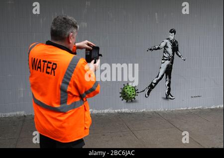 Eine Person nimmt ein Bild von einem Kunststück des Künstlers auf, das als Rebel Bear bekannt ist, nachdem es an einer Wand in der Bath Street in Glasgow auftauchte. Die neue Ergänzung zu Glasgows Straßenkunst erfasst die globale Coronavirus Krise. Das Stück zeigt einen Mann, der eine Kette mit einem daran befestigten Keim zieht, während Großbritannien sich in einem Lockdown fortsetzt, um die Ausbreitung des Coronavirus einzudämmen. Stockfoto
