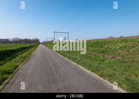 Asphaltstraße in der Nähe der Eisenbahn in der Landschaft Belgiens. Stockfoto