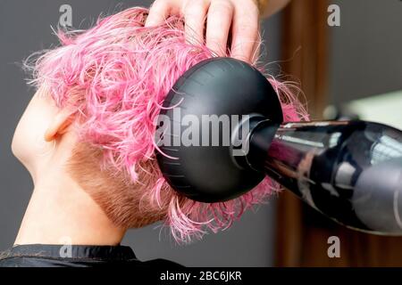 Die Hände des Friseursalons trocknet die rosafarbenen Haare der Frau aus der Nähe. Stockfoto