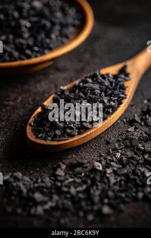 Nahaufnahme von schwarzen Salzkristallen in Holzlöffel auf schwarzem Grund Stockfoto