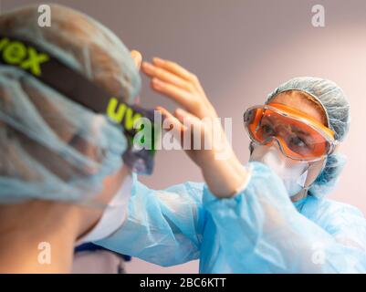 Dresden, Deutschland. April 2020. ABBILDUNG - Zahnmediziner helfen sich gegenseitig, eine Schutzbrille zu setzen, bevor sie einen Corona-Patienten in einem Zahnbüro behandeln (Szene gestellt). Kredit: Robert Michael / dpa-Zentralbild / dpa / Alamy Live News Stockfoto