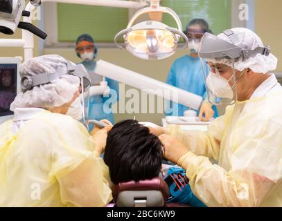 Dresden, Deutschland. April 2020. ABBILDUNG - Zahnarzt Conrad Kühnöl (r) behandelt in seiner Zahnarztpraxis (posierte Szene) einen Corona-Patienten mit Visier, FFP3-Beatmungsmaske und antiviralem Gown zusammen mit seinen Zahnarzthelfern. Kredit: Robert Michael / dpa-Zentralbild / dpa / Alamy Live News Stockfoto