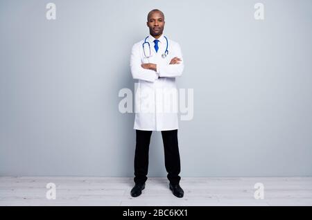 Ganzkörperfoto des professionellen Hausarztes dunkler Hauttyp Treffen Patienten Virologe Arme gekreuzt tragen weiße lange Labor-Mantel Krawatte Hosen Schuhe Stockfoto