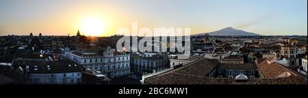Catania, Sizilien in Italien. Luftaufnahme der Dächer der Stadt bei Sonnenuntergang mit dem unglaublichen Vulkan Ätna, der im Hintergrund raucht, schöne warme Farben Stockfoto