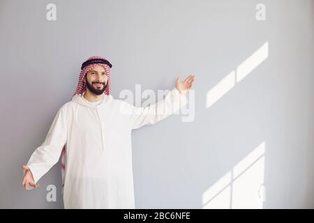 Der attraktive lächelnde arabische Mann zeigt seine Hand auf einen grauen Hintergrund Stockfoto
