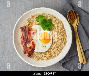 Haferbrei, gebratenes Ei und gebratener Speck. Herzhaftes fettes, kalorienreiches Frühstück, Energiequelle. Stockfoto