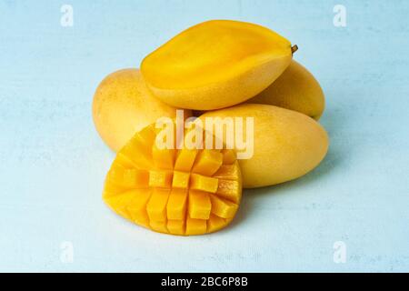 Vier ganze Mango-Früchte auf hellblauem Tisch und in Scheiben geschnitten. Große saftige gelbe Früchte Stockfoto