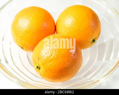 Drei Orangen in einer Glasschale auf einer weißen Tischdecke Stockfoto