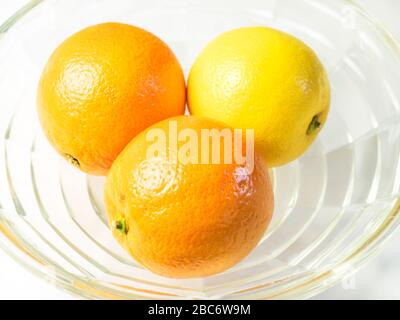 Zwei Orangen und eine Zitrone in einer Glasschale auf einer weißen Tischdecke Stockfoto