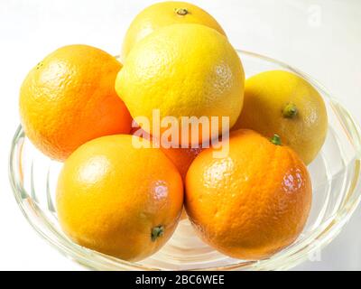 Orangen und Zitronen in einer gläsernen Fruchtschale auf einem weißen Tischtuch Stockfoto