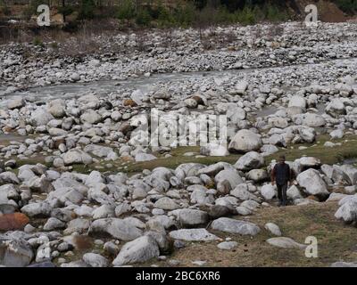 Manali, Himachal Pradesh- März 2018: Ein Mann spaziert am Beas-Fluss in Manali unter die Felsen. Stockfoto