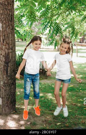 Zwei kleine Mädchen in weißen T-Shirts springen im Park im Freien. Stockfoto