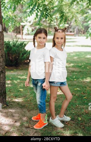 Zwei kleine Mädchen in weißen T-Shirts stehen im Park im Freien. Verspotten Sie sich. Stockfoto