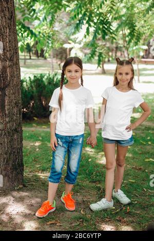 Zwei kleine Mädchen in weißen T-Shirts stehen im Park im Freien. Verspotten Sie sich. Stockfoto