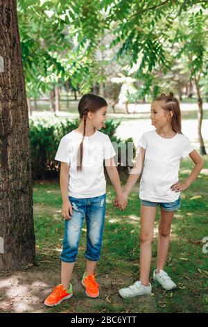 Zwei kleine Mädchen in weißen T-Shirts stehen im Park im Freien. Verspotten Sie sich. Stockfoto