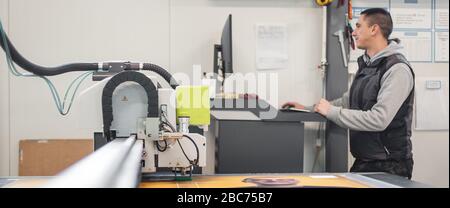 Der Techniker der Druckerei arbeitet an einer großen CNC-Computer- numerischen Steuerungs- und Schneidemaschine Stockfoto