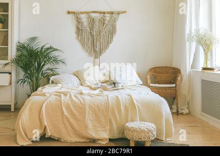 Modernes, romantisches zimmer im scandi boho Stil mit dekorativen Kissen, grüner Anlage und einer makramen Wandverkleidung. Leichtes, warmes, gemütliches, komfortables Zuhause. Stockfoto