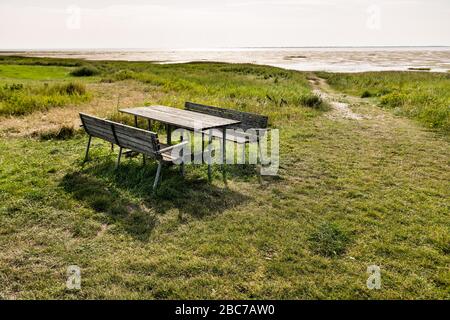 Picknicktisch mit zwei Holzbänken auf einer grünen Wiese mit Blick auf das Wattenmeer in der Sonne. Stockfoto