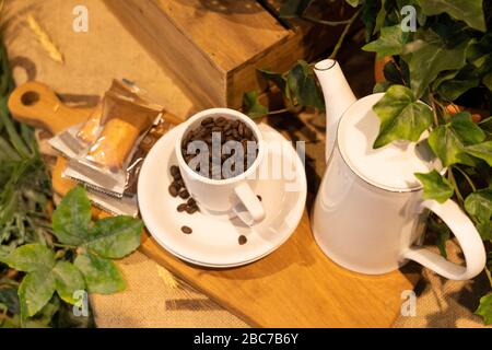 Schwarzer Kaffee auf einer Teetase mit Brot und Pflanzendekorationen. Kaffee von oben mit Teetake und Kaffeebohnen auf einem Holztisch. Stockfoto