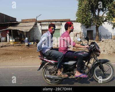 Agra, Uttar Pradesh, Indien - März 2018: Zwei Männer sprangen mit Farben für das Holi Festival Celebration Ride a Motorcyle in Tandem. Stockfoto
