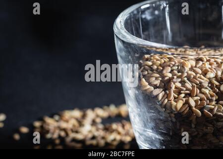 Nahaufnahme von organischen ganzen Sesamsamen, in einem kleinen Glasbecher auf schwarzem Grund Stockfoto