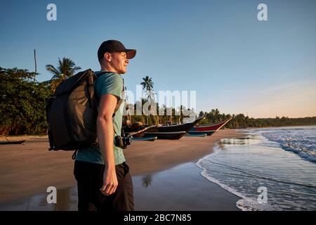 Junger Mann mit Rucksack am tropischen Strand. Küste Sri Lankas am Morgen leicht. Stockfoto