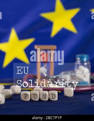 Worte aus Holzbriefen zusammengesetzter EU-SOLIDARITÄTSFONDS. EU-Flagge im Hintergrund. Nahaufnahme Stockfoto