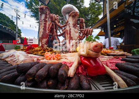 Auf einem großen Grillplatz werden ein saugerndes Schwein und verschiedene Wurstsorten gezeigt Stockfoto