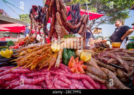 Auf einem großen Grillplatz werden ein saugerndes Schwein und verschiedene Wurstsorten gezeigt Stockfoto