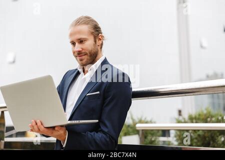 Gutaussehender, junger bärtiger Geschäftsmann, der draußen auf der Straße steht und an einem Laptop arbeitet Stockfoto