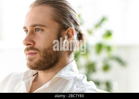 Foto des jungen gutaussehenden Geschäftsmannes, der weißes Hemd und Ohrstöpsel in der Wohnung trägt Stockfoto