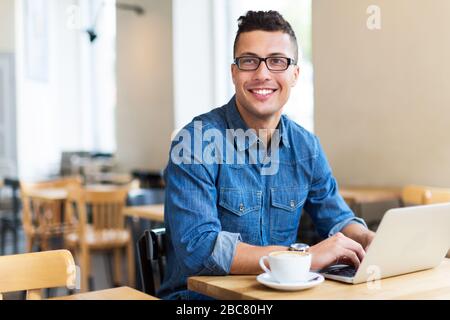 Junger Mann mit Laptop im Cafe Stockfoto