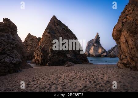 Beeindruckender Strand von Ursa mit einzigartigem Felsen, der von goldenem Abendlicht bei Sonnenuntergang beleuchtet wird. Das Hotel liegt in der Nähe von Cabo da Roca, Sintra an der Küste des Atlantiks in Portugal. Stockfoto