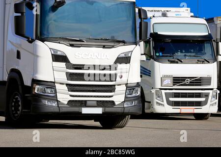 Zwei weiße, auf einem Lkw-Stopp geparkte Scania- und Volvo-Kühltransport-Güterwagen schließen sich. Salo, Finnland. April 2019 Stockfoto