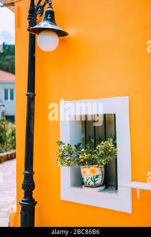 Typisches griechisches Architektur-Detailkonzept. Orangefarbene Hauswand, Blumen in den Töpfen, Laterne, traditionelles Haus in Griechenland. Stockfoto