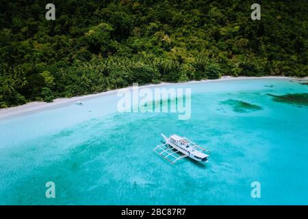 Luftdrone mit Blick auf einen weitläufigen tropischen Strand mit üppigem Regenwald und banca-booten. Urlaub verträumter Ort rohes Paradies. Stockfoto