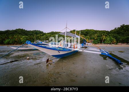 Das philippinische Boot Banca. Traditionelles Fischerboot am Strand bei Ebbe in Abendlicht. El Nido, Palawan. Stockfoto
