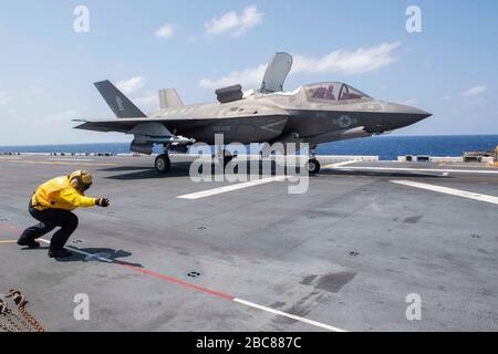 Eine gelbe Jacke der US-Marine leitet einen Stealth-Kämpfer des Marine Corps F-35B Lightning II, der der 31. Marine Expeditionary Unit zugeordnet ist, zum Start vom Flugdeck des amphibischen Angriffsschiffs der amerikanischen Klasse USS America bei Routineoperationen am 25. März 2020 in der philippinischen See. Stockfoto