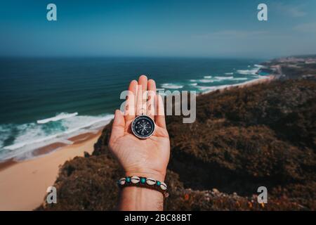 POV Mann hand mit Kompass. Symbolling Abenteuer - Konzept gegen das Meer und die Wellen an die Küste im Hintergrund. Stockfoto