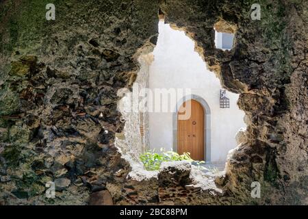 Blick auf eine Holztür eines neuen Hauses durch die Öffnung in der Wand eines alten zerstörten Gebäudes. Stockfoto