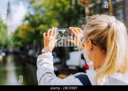 Frau Tourist, der ein Bild von Canal in Amsterdam auf dem Mobiltelefon. Warme gold Nachmittag Sonne. Reisen in Europa. Stockfoto