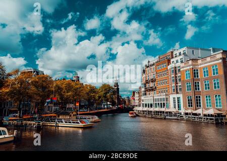 Blick auf die Stadt von Amsterdam mit Kreuzfahrtschiffen und die typischen Backsteinhäuser an einem sonnigen Tag mit lebendigen Fluffy Clouds. Stockfoto