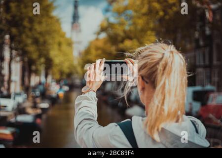 Frau Tourist, der ein Bild von Canal in Amsterdam auf dem Mobiltelefon. Warme gold Nachmittag Sonne. Reisen in Europa. Stockfoto