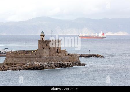 Ein Schiff segelt vor Rhodos, Griechenland. Im Vordergrund steht das Fort of St Nicholas, ein befestigter Turm. Stockfoto