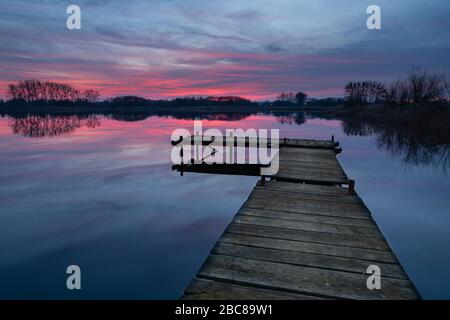 Angelpier aus Holz am ruhigen See und bunte Wolken nach Sonnenuntergang Stockfoto