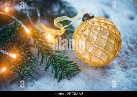 Golden Christmas Ball mit Band auf Schnee in der Nähe tanne Zweig mit helle Girlande. Festliche Hintergrund mit kopieren. Stockfoto