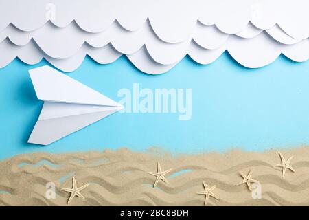 Papierwolken und Flugzeug, Sand mit Starfischen auf blauem Grund. Urlaub Stockfoto