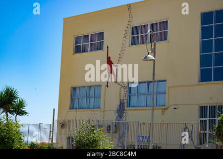 Straßenkunst eines Jungen in einem roten Mantel, der eine Leiter in Heraklion, Kreta klettert Stockfoto